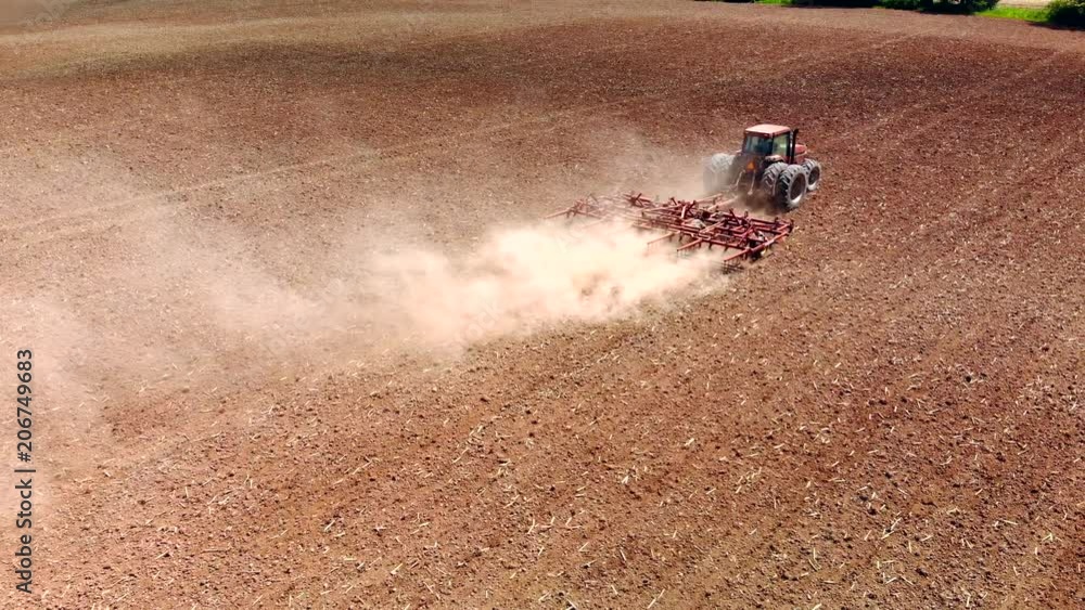 Big farm tractor tilling dusty Springtime fields, aerial view.

