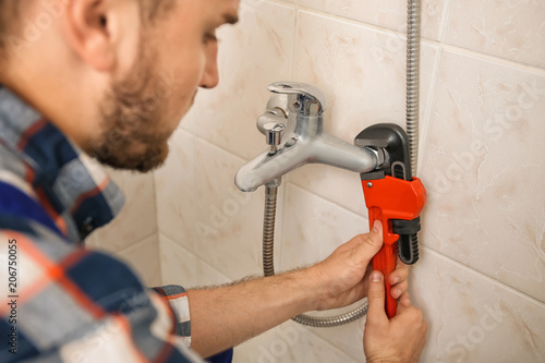 Professional plumber fixing bath tap indoors, closeup