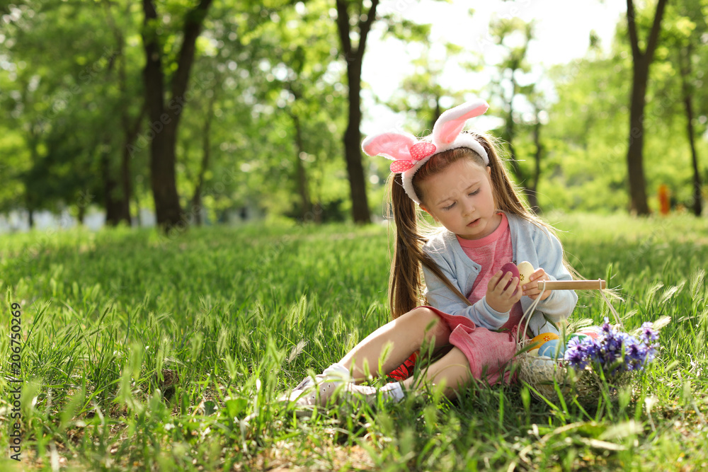 Little girl with bunny ears and basket full of Easter eggs outdoors Little girl with bunny ears and basket full of Easter eggs outdoors
