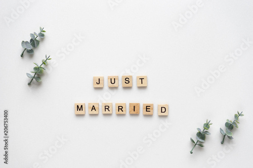 Wooden letters  speling just married with oregano branches on white marble. Top view. photo