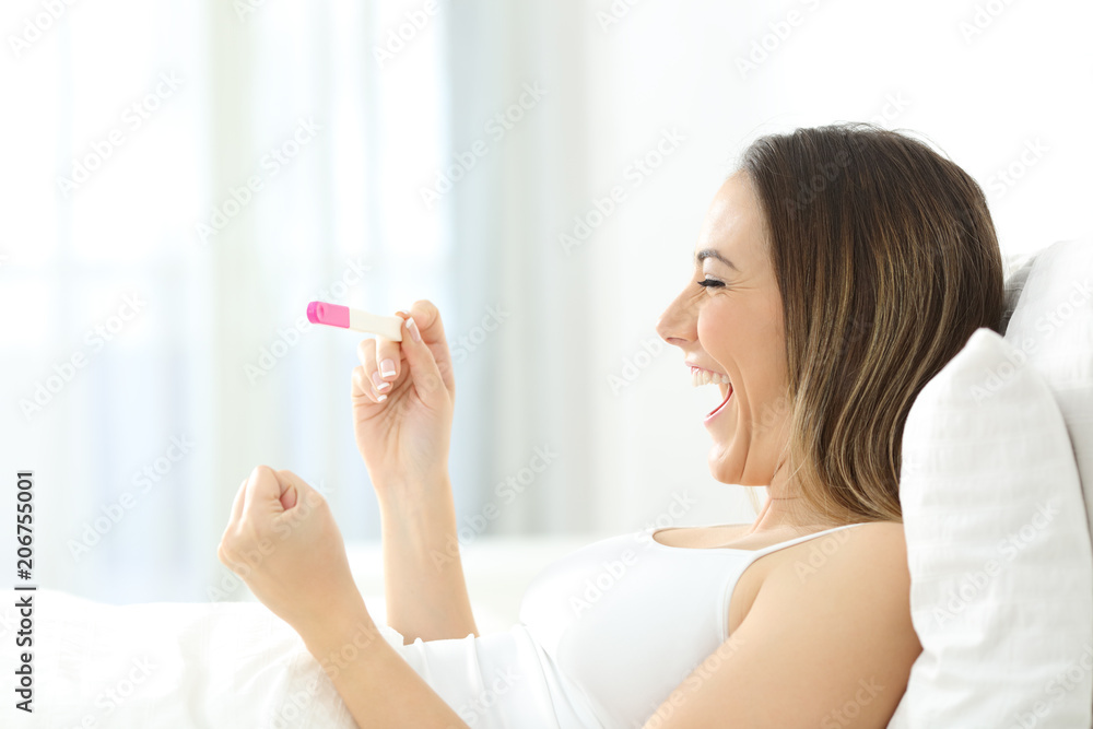 Excited woman checking a positive pregnancy test in the bed Excited woman checking a positive pregnancy test in the bed