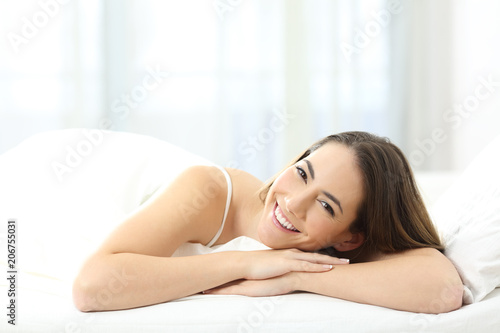 Happy woman looking at camera on a bed in the morning
