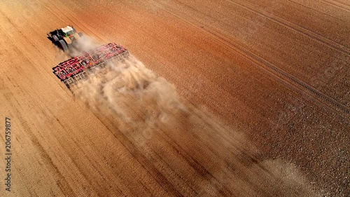 Big farm tractor tilling dusty Springtime fields, aerial view.
