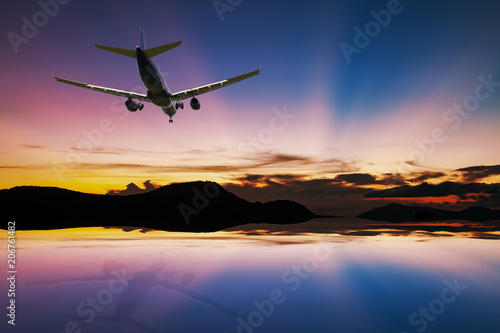 Airplane flying over tropical sea at beautiful light sunset or sunrise with reflex in the water at phuket thailand scenery background.