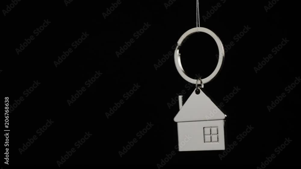 Metal key holder with house shape hanging and rotating on black background Metal key holder with house shape hanging and rotating on black background
