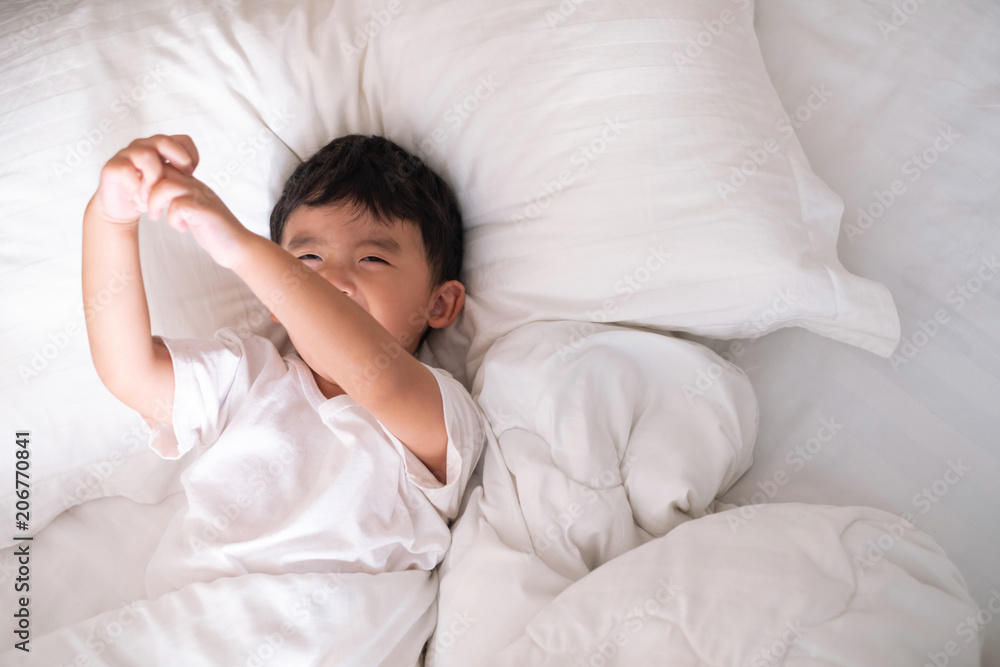 3 years old little cute Asian boy at home on the bed, kid lying playing and smiling on white bed with pillow and blanket, top view with copy space.