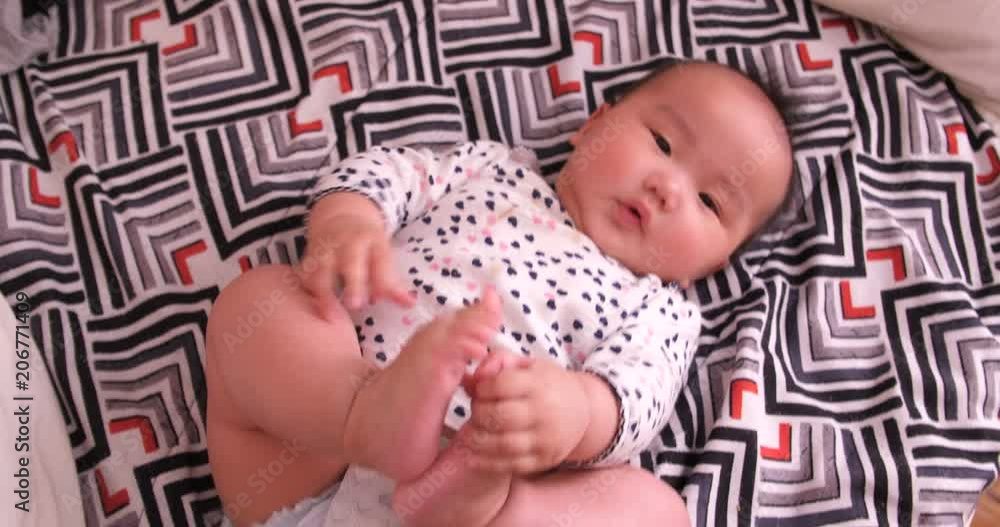 Asain baby girl laying on the bed sneezing and holding onto her feet while playing Asain baby girl laying on the bed sneezing and holding onto her feet while playing