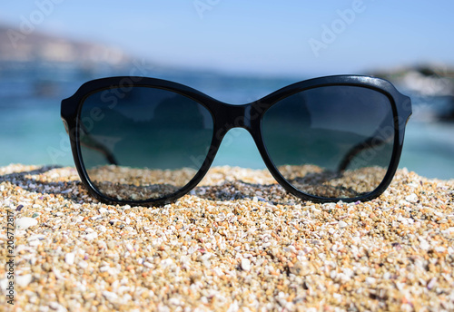 Front view of sunglasses on the beach near the blue sea with sand