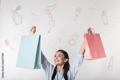 Loving shopping. Cheerful emotional young woman looking excited and putting her paper bags up while going shopping