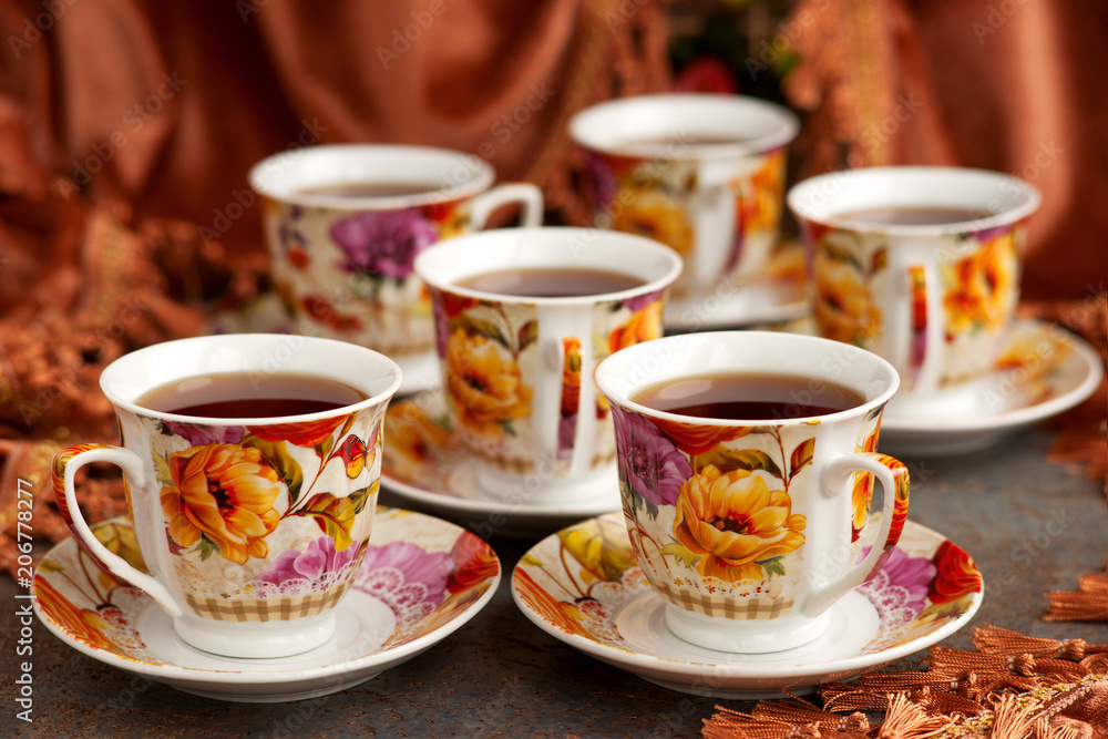 Tea set in brown and red tones. Six cups of tea on the background of velvet curtains. A set of bright mugs for spring and summer mood. Tea set in brown and red tones. Six cups of tea on the background of velvet curtains. A set of bright mugs for spring and summer mood.