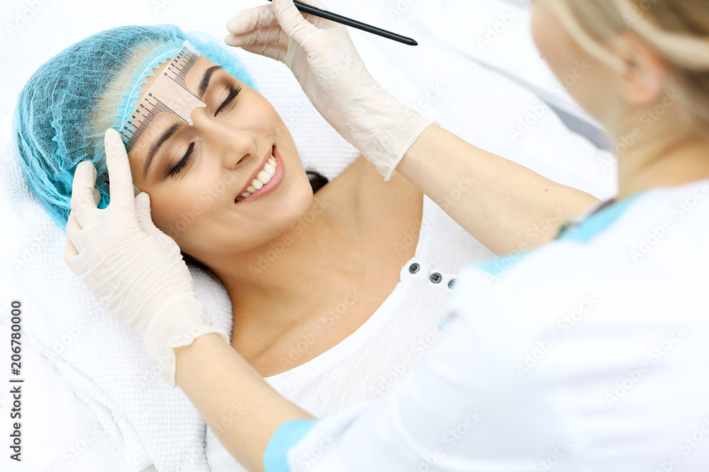 Professional beautician is going to correct eyebrow line at woman face using cosmetic ruler. Permanent brow makeup in beauty salon, closeup. Cosmetology treatment Professional beautician is going to correct eyebrow line at woman face using cosmetic ruler. Permanent brow makeup in beauty salon, closeup. Cosmetology treatment