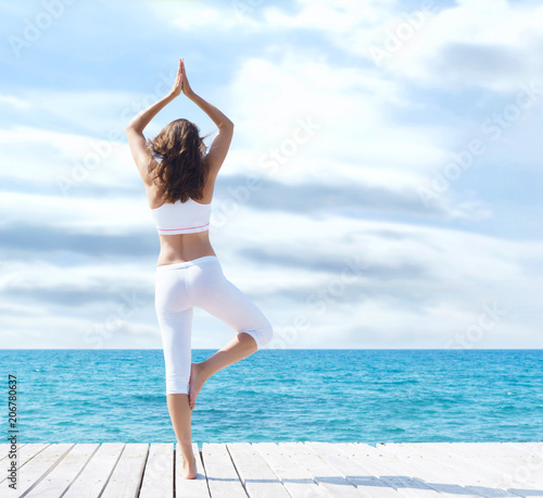 Attractive woman in white sporty clothes doing yoga on a wooden pier. Yoga, sport, leisure, recreation and freedom.