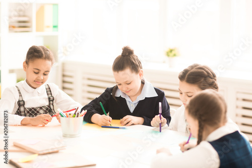 Group of schoolgirls draw with crayons together at the table