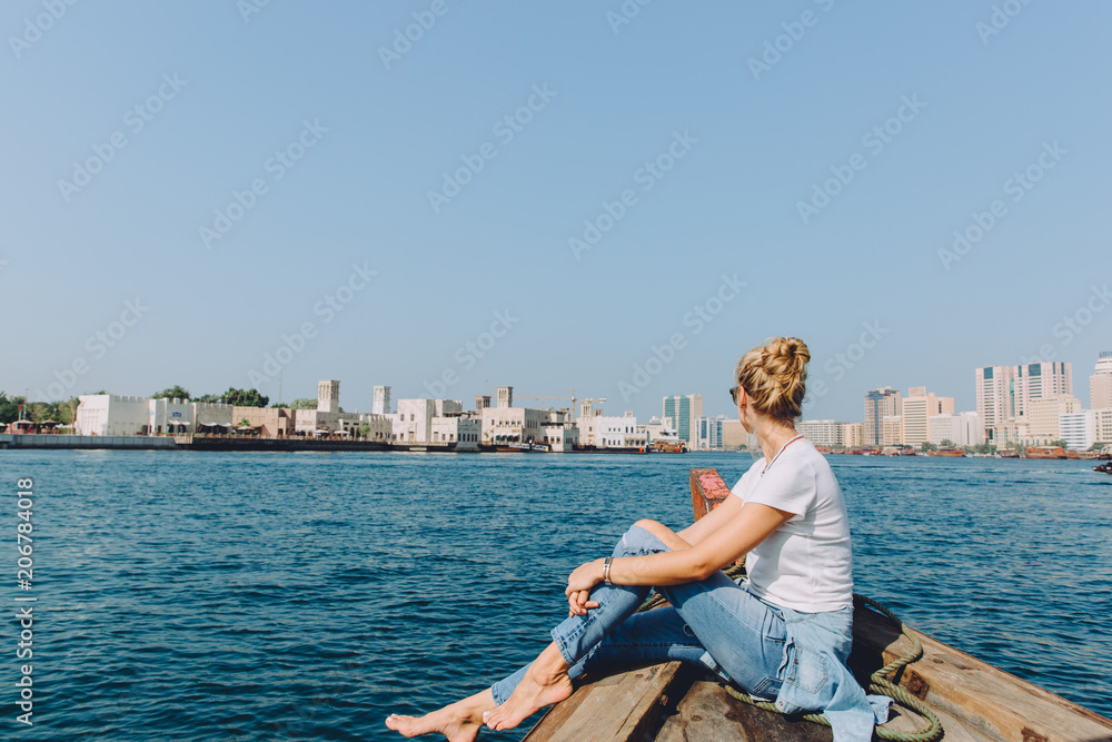Young beautiful blonde woman sitting at boat and looking at sea and the city