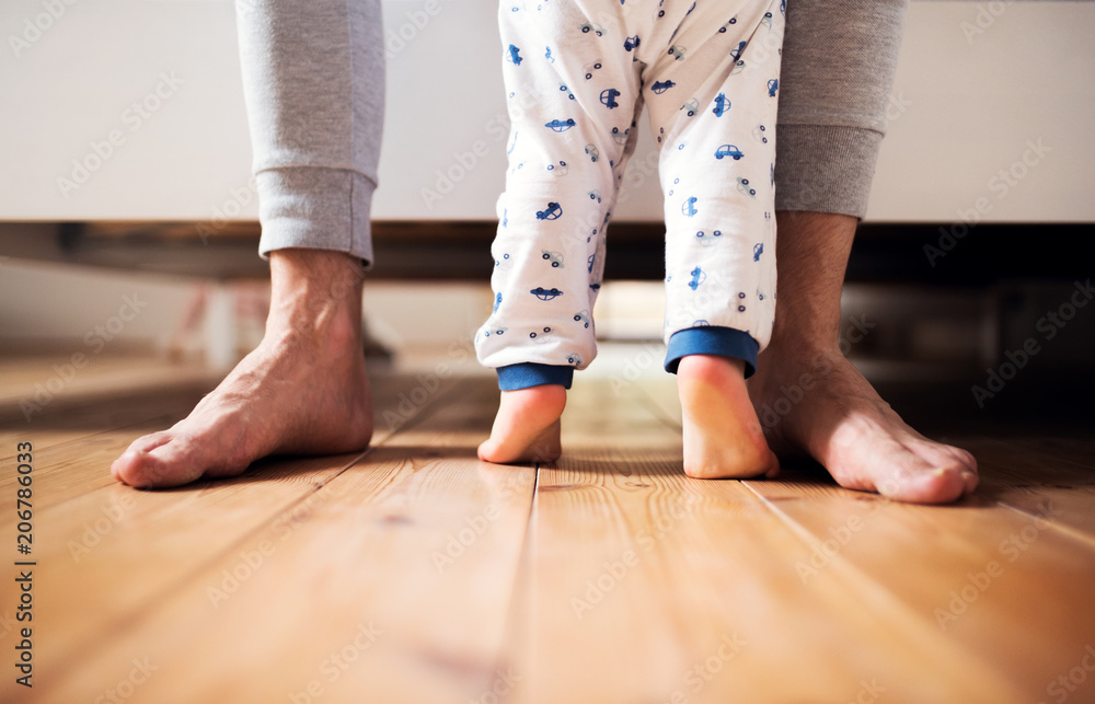 Legs of father and a toddler boy standing on the floor in bedroom at home. Legs of father and a toddler boy standing on the floor in bedroom at home.