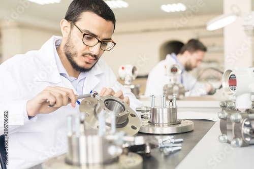 Serious concentrated handsome young Arabian technical assembler using wrench while making manometer bearing in workshop