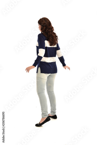 full length portrait of girl wearing striped blue and white jumper and jeans. standing pose facing away from the camera, on white studio background
