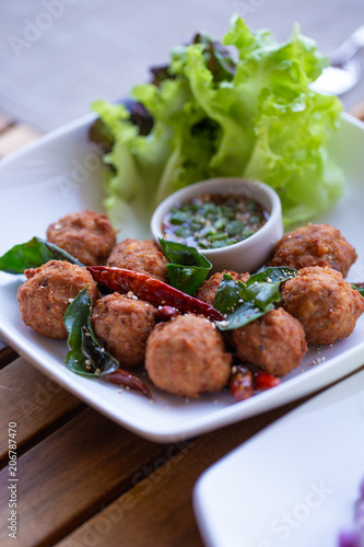 A dish of Thai style fried spicy ground pork ball served with spicy shallot sauce decorated with fried kaffir lime leaf and chilli.