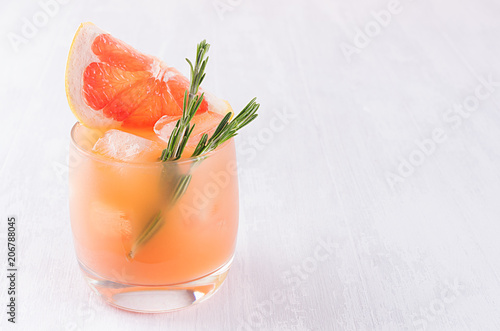 Cold detox cocktail of grapefruit juice with ice, rosemary, slices citrus on soft light white wood background.