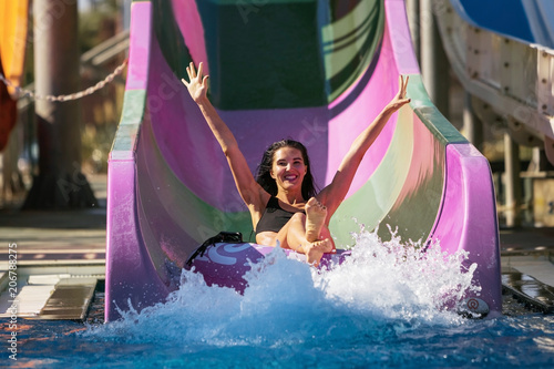 pretty brunette slim woman with raised hands on the rubber ring having fun coming down on the purple water slide in the aqua park. Summer Vacation. Weekend on resort photo