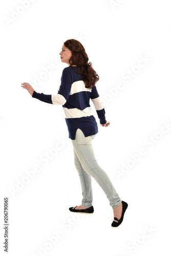 full length portrait of girl wearing striped blue and white jumper and jeans. standing pose facing away from the camera, on white studio background