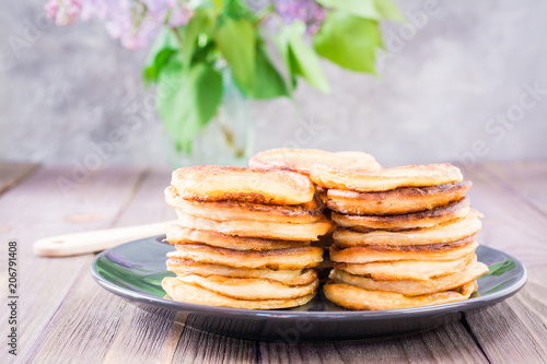 A pile of pancakes on a plate and a bouquet of lilac in a vase on a wooden table