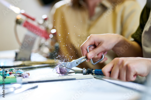 Close up of unrecognizable female artist breaking glass ball shattering it with shard flying up while making beads in glassworking studio, copy space