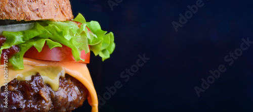 Burger flyer. Cheese burger with grilled meat, cheese, tomato, salad and onion rings. Close-up of delicious fresh home made burger with salad and cheese on bark blue background photo