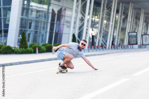 Wallpaper Mural Skateboarder in sunglasses rides longboard on asphalt road before modern building in the city, low position trick ride Torontodigital.ca