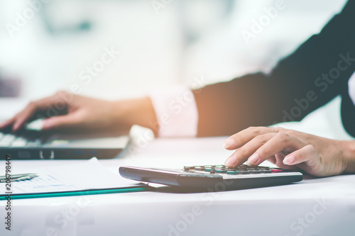 A business woman analyzing investment charts at workplace and using laptop and touch calculator.