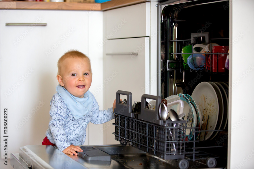 Toddler child, boy, helping mom, putting dirty dishes in dishwasher at home, . Toddler child, boy, helping mom, putting dirty dishes in dishwasher at home, .