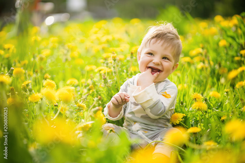 Concept: family values. Portrait of adorable innocent brown-eyed baby play outdoor in the sunny dandelions field and making funny faces.