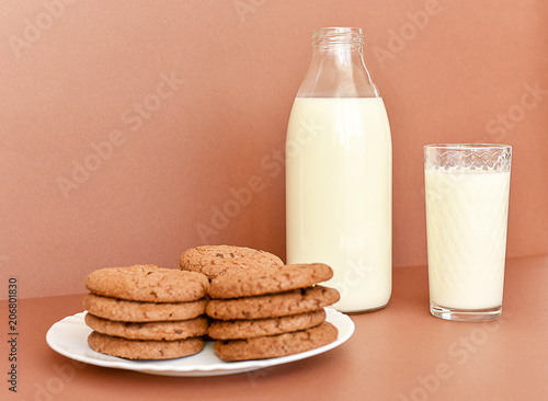 Milk in glass bottle and transparent glass and cookies on white plate 