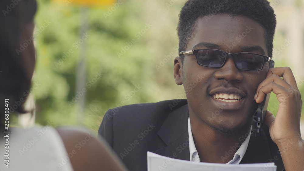 Young positive afro american entrepreneur in trendy eyewear having phone conversation with secretary assistant giving task for day finding out schedule planning of important meetings Young positive afro american entrepreneur in trendy eyewear having phone conversation with secretary assistant giving task for day finding out schedule planning of important meetings