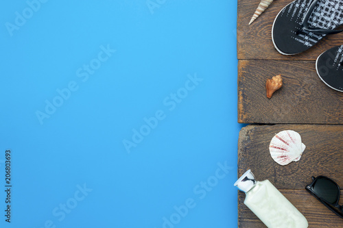 Table top view aerial image of items to travel summer holiday background concept.Flat lay essentials accessory for travel to beach trip.Fashion sun glasses with slipper on plank wooden with blue paper