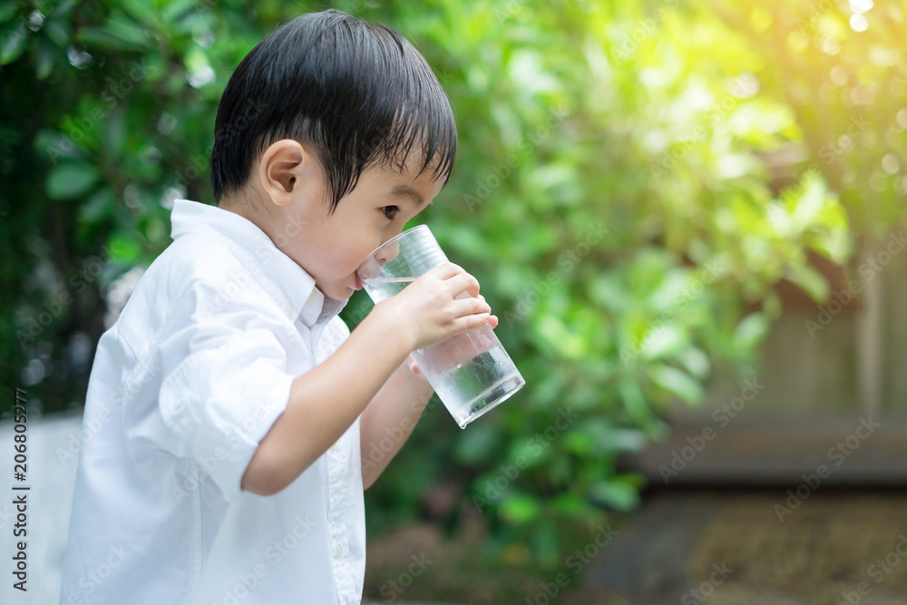 Asian Cute boy wear white shirt drinking cold water from glass in green nature background
