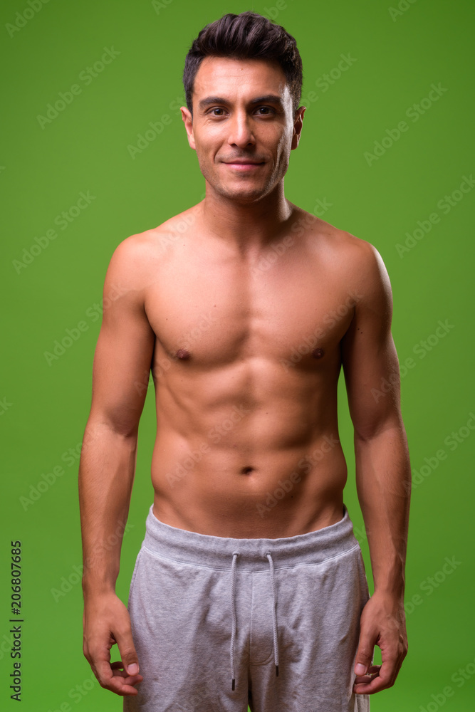 Fototapeta premium Young handsome Hispanic man shirtless against green background