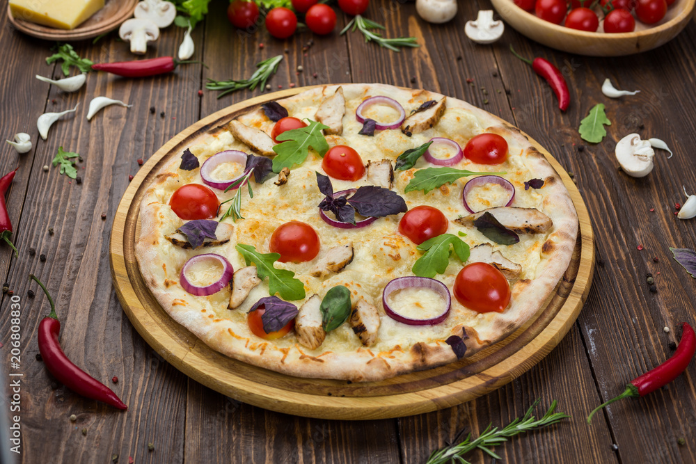 Italian Pizza with chicken, cherry tomatoes, cheese and onions on the board decorated with leaves of arugula and basil Italian Pizza with chicken, cherry tomatoes, cheese and onions on the board decorated with leaves of arugula and basil