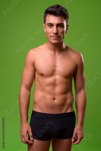 Young handsome Hispanic man shirtless against green background