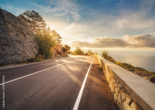 Mountain road at sunset in Europe. Landscape with rocks, sunny sky with clouds and beautiful asphalt road in the evening in summer. Colorful travel background. Highway in mountains. Transportation photo