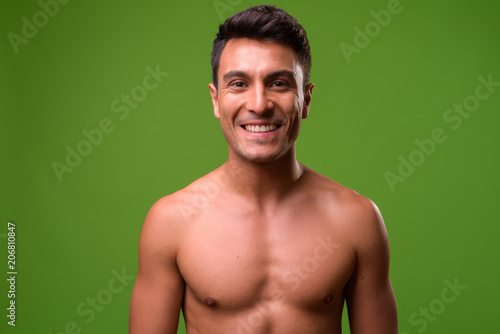 Young handsome Hispanic man shirtless against green background