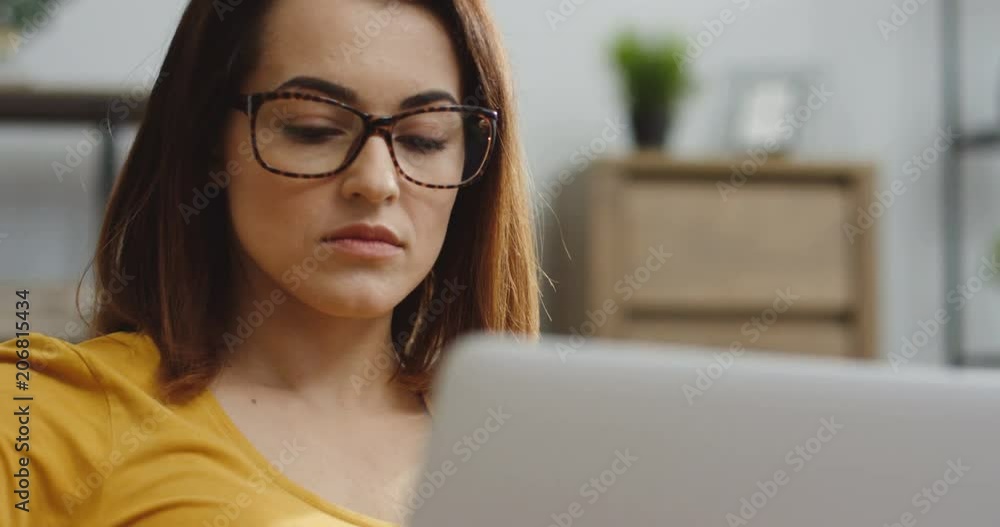 Close up of the Caucasian woman in the yellow blouse taking on the glasses and starting to type on the laptop computer. Inside Close up of the Caucasian woman in the yellow blouse taking on the glasses and starting to type on the laptop computer. Inside