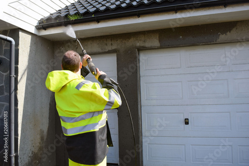 The man cleans the walls from the side of the street with the help of a stream of water under pressure.