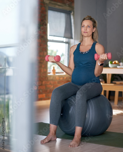Pregnant woman on exercise ball holding weights, healthy fitness