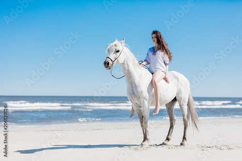 Girl sitting on a white horse by the sea