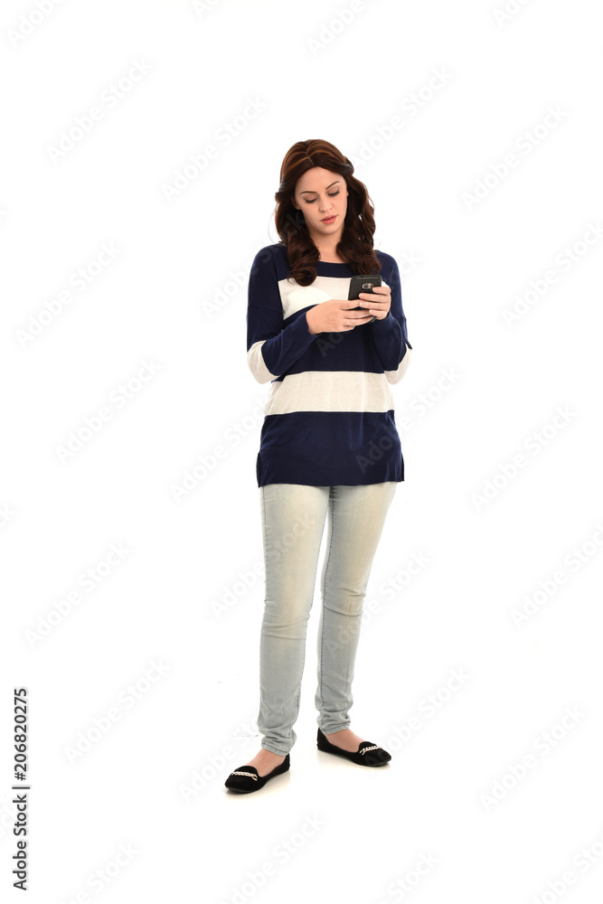 full length portrait of girl wearing striped blue and white jumper and jeans, holding a phone. standing pose on white studio background full length portrait of girl wearing striped blue and white jumper and jeans, holding a phone. standing pose on white studio background