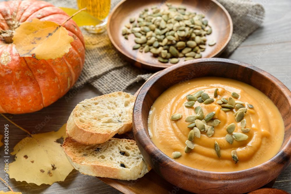 Pumpkin soup in a wooden bowl, with autumn leaves and pumpkin Pumpkin soup in a wooden bowl, with autumn leaves and pumpkin