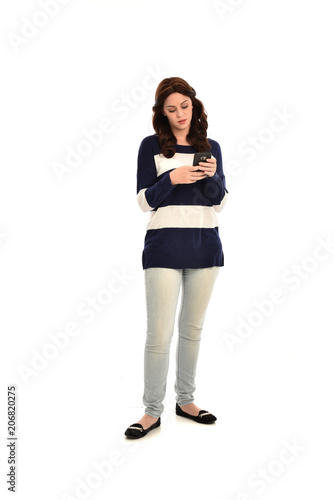 full length portrait of girl wearing striped blue and white jumper and jeans, holding a phone. standing pose on white studio background © faestock