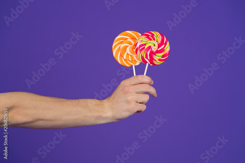 Candies on stick on violet background. Lollipops in hand on purple background. Sweet candy swirls. Food or snack and dessert eating. Sweet shop concept, copy space. punchy pastels