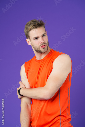 Man on thoughtful face posing in sportive clothes, violet background. Guy with bristle wears sportive shirt and fitness tracker. Sporty accessories concept. Man with modern digital sporty accessory